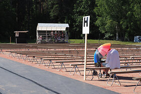 Yksittäinen istuja juhlakentällä aurinkovarjo suojanaan, taustalla kuorokatos